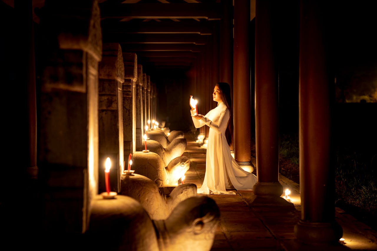 A woman in traditional Ao Dai holding a candle in a dimly lit temple in Hue, Vietnam, creating an atmospheric scene.